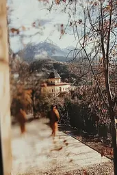 Midjourney generated image using SREF code Rustlight: A person walking down a path in front of a building.