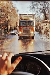 Midjourney generated image using SREF code Rustlight: A man driving a semi truck on a wet road.