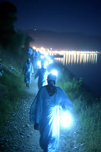 Midjourney generated image using SREF code Haloed Spectres: A group of people walking down a dirt road at night.