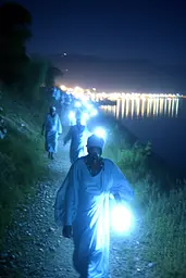 Midjourney generated image using SREF code Haloed Spectres: A group of people walking down a dirt road at night.