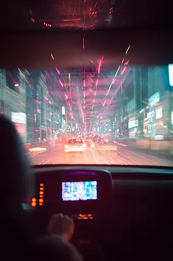 Midjourney generated image using SREF code Cyan Flux: A view of a city street at night from inside a car.