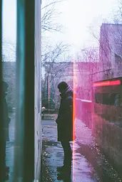 Midjourney generated image using SREF code Cyan Flux: A person standing in the rain looking out of a window.