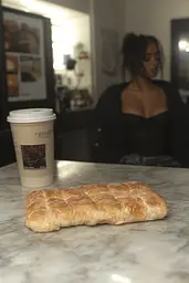 Midjourney generated image using SREF code Hushframe: A loaf of bread sitting on top of a counter next to a cup of coffee.