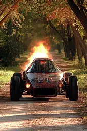 Midjourney generated image using SREF code Obscuralume: A car with flames coming out of it driving down a dirt road.