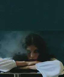 Midjourney generated image using SREF code Gossamer Gaze, Ominous Alienscape, Ethereal Echoes: A woman sitting at a table with her head resting on her hands.