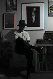 Midjourney generated image using SREF code Opaque Lenses: A man sitting on a chair in front of a record player.