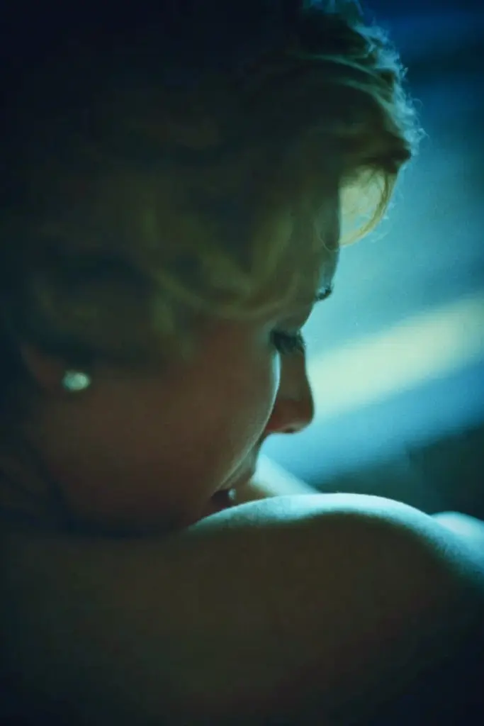 Midjourney generated image using SREF code Blue Velvet: A woman with blonde hair is looking out the window.