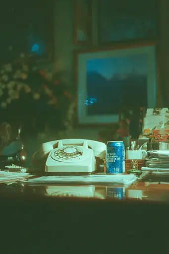 Midjourney generated image using SREF code Blue Velvet: A can of beer sitting on top of a desk next to a telephone.