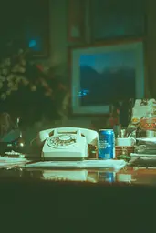 Midjourney generated image using SREF code Blue Velvet: A can of beer sitting on top of a desk next to a telephone.