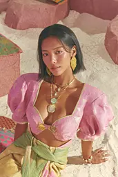 Midjourney generated image using SREF code Plastisphere: a woman in a pink top and green skirt sitting on a beach