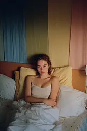 Midjourney generated image using SREF code Hushed Loomlight: A woman sitting on a bed in a bedroom.