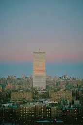 Midjourney generated image using SREF code Hushed Loomlight: A tall building in the middle of a city at dusk.