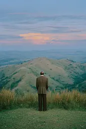 Midjourney generated image using SREF code Hushed Loomlight: A man in a suit standing on top of a hill.