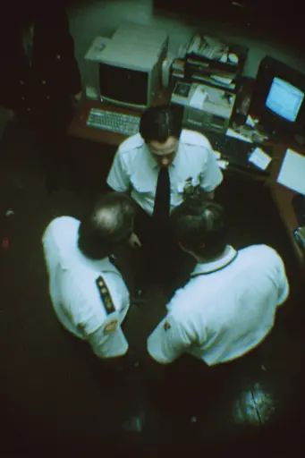 Midjourney generated image using SREF code Glitchmorose: A group of men standing around a desk in an office.