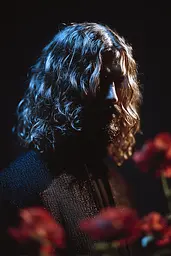 Midjourney generated image using SREF code Flarevox: A man with long hair standing in front of flowers.